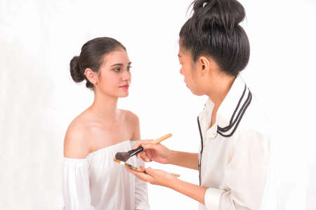 Beautiful woman with a makeup artist preparing a brush on white background.の写真素材