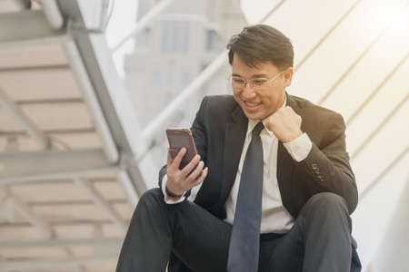 Middle-aged business man looking at smartphone in his hand while sitting on the stair in city.の写真素材