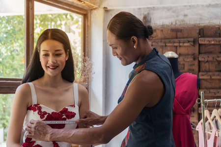 Fashion designers is measuring beautiful young woman in the studio.