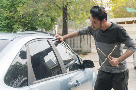 Young man holding socket wrench tool to break the car mirror. Asian young man trying to steal a car.の写真素材