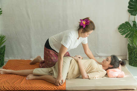 Concept thai Massage. Beautiful Asian young woman getting thai herbal massage in spa salon.Thai girl stretching her legs with masseur.の写真素材