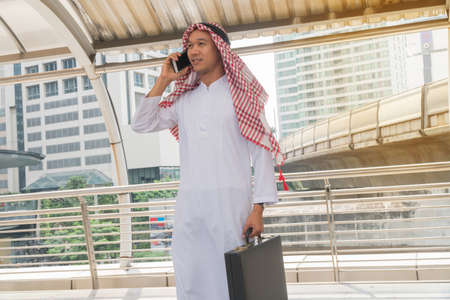 Muslim businessmen talking mobile phones. Young Arab businessman holding briefcase in a modern city...