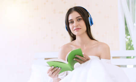 Cheerful smile young woman listening music with headphones holding book in her hands feeling relax...