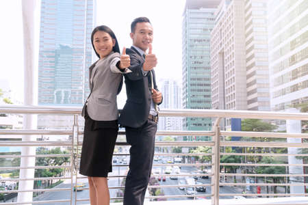 Smiling Business couple wear suit showing their thumb up together represent business success, ok, great, all good things and like in the modern city. Successful business and teamwork concept.の写真素材