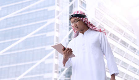 Arab Middle Eastern young businessman holding digital tablet while looking business data feed in his...
