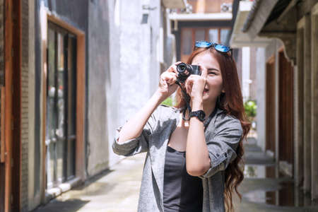 Cheerful photographer young woman with sunglasses holding camera taking photo in city. Traveler...