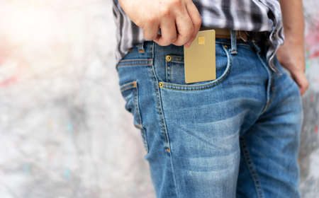 Hands of young man pick up empty gold generic credit card out of jeans pocket. Concept of losing money, business and finance.の写真素材