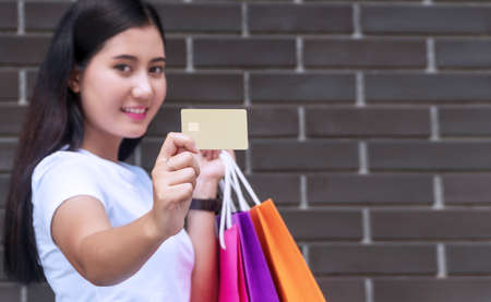 Joyful young woman holding shopping bags and blank credit card on concrete walls background with...
