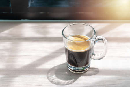Hot Black coffee in glass beside window of the morning on wooden background with copy space.の写真素材