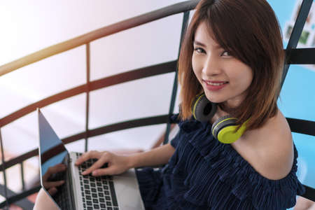 Cheerful smiling young woman with earphones holding laptop in her hand while looking to camera at home. Lifestyle relaxing concept.の写真素材