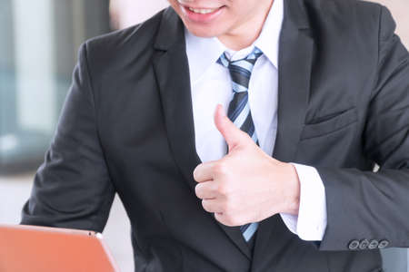 Businessman raised thumb up while working for good job. Young man wear suit showing his thumb up...