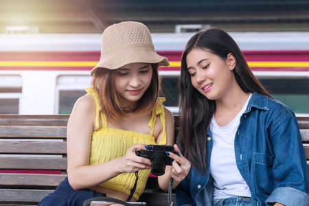 Travel and lifestyle concept. Two young woman friends watching photos on digital camera in the station. Traveller cheerful girl watching shocked photos on camera laughing at the railway station.の写真素材