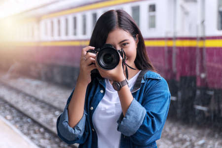 Photographer young woman taking pictures holding digital camera in station. Attractive girl travel with her camera in train station on rainy day.の写真素材