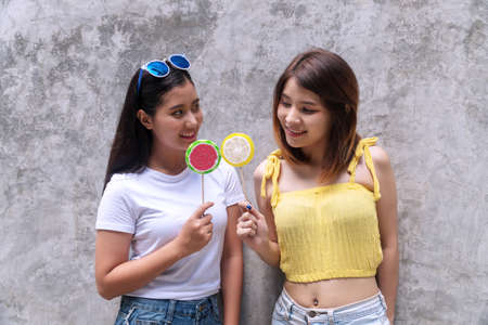 Lifestyle concept. Happy smile two young women holding lollipop looking each other on grey background. Cheerful girl with sunglasses holding candy in her hand looking at her friend.の写真素材