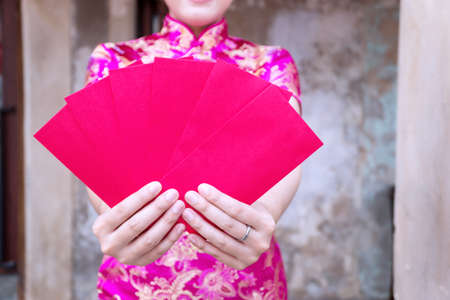 Attractive happy young woman wear cheongsam deep pink dress holding red envelopes containing money for luck and prosperity family give for her. Chinese New Year celebrations conceptの写真素材