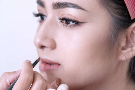 Close up beautiful pretty young woman with hands beautician or makeup artist applying lipstick on her face in studio.の写真素材