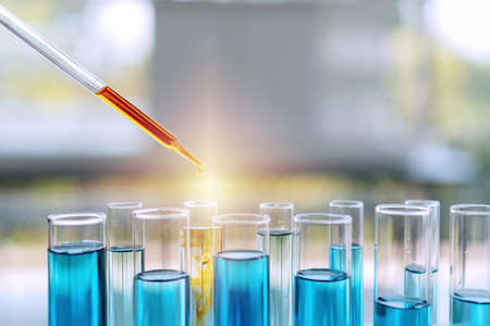 The test tube of science. Laboratory pipette with drop of orange liquid over test tubes filled with blue chemical solution for an experiment in science research lab.の写真素材