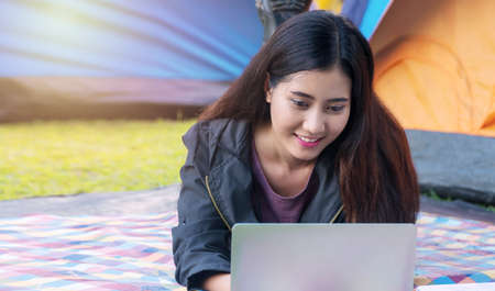 Traveller young woman using laptop shopping online at camping zone. Cheerful smiling girl relaxing on vacation. Lifestyle travel concept.の写真素材
