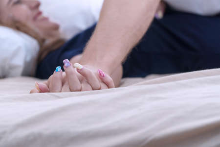 Focus hands young man holding his girlfriend lying on the bed. Passionate couple enjoying sensual foreplay before having sex or making love in bedroom. Concept relationship.の写真素材