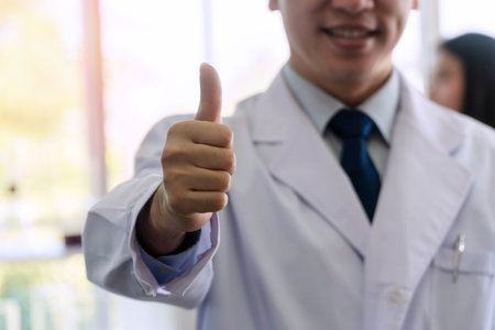 Hands of doctor in white coat with pen showing thumbs up while working success in hospital. Healthcare concept. Focus hands.の写真素材