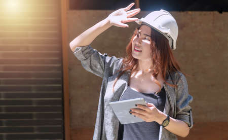 Engineer young woman wearing white helmet stand at outdoor holding tablet on site job. Architect...