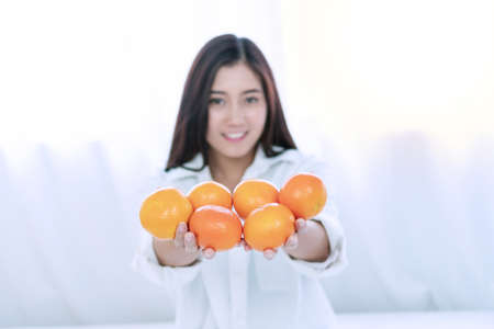 Lifestyle and healthy food concept. Focus hands of smile young woman holding fresh oranges fruit in her hand on white bed at home with copy space. Focus oranges fruit.の写真素材
