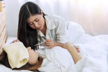 Sick woman have good friend to take care of her, having temperature check with thermometer. Young...