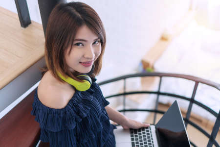 Cheerful smiling young woman with earphones holding laptop in her hand while looking to camera at home. Lifestyle relaxing concept.の写真素材