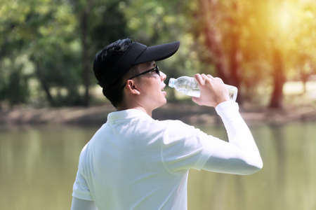 Golfer man drinking of fresh water with bottle while thirsty and tired. Young men wearing white...