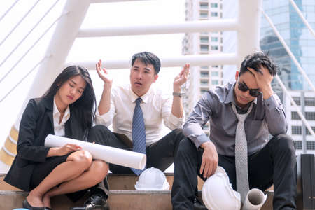 Group architect or business people feeling tired and headache with their job. sitting on stairs with safety helmet and blue print on their hand. business failure and unemployment problem concept.の写真素材