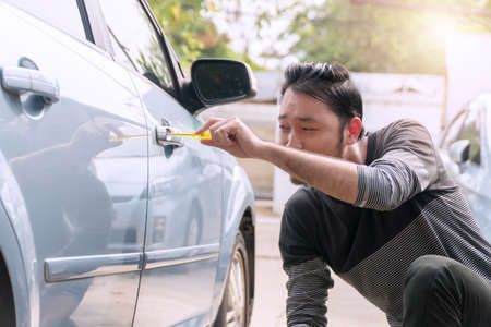 Man using screwdriver open car door. Thief male stealing secretly used screwdriver to open the car door in parking. Car robbery concept.の写真素材