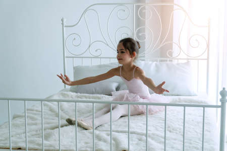 Cute pink dresses little girl 9 year dancing ballet with white bed in bedroom at home, Ballerina young girl practicing ballet dance at room. Kid ballet and performance art for modern concept.の写真素材