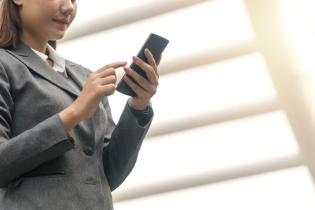 Businesswoman using smartphone in her hand while working on internet.  Young woman wearing suit while chatting digital mobile on through application at urban city.の写真素材