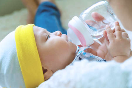 Portrait cute baby boy drinking water from bottle with his mom. Hand of asian young woman holding bottle with water while feeding aqua for her son. Lifestyle child concept.の写真素材