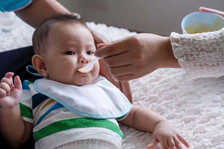 Portrait cute baby boy lying on the lap of his father while hand of his mother holding spoon feeding food for his. Asian young woman feed male for her son. Lifestyle child concept.の写真素材