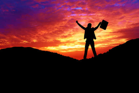 Silhouette of professional businessman wear suit celebrating success raised arm while standing on the mountain with sunrise. Active lifestyle concept.の写真素材