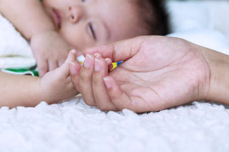 Cute baby boy sleeping on white bed with hand of mother holding his hand. Focus hand. Lifestyle...