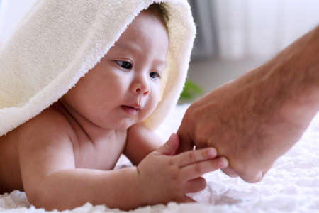 Cheerful cute baby looking at hand his father under white blanket. Innocence baby with parent...