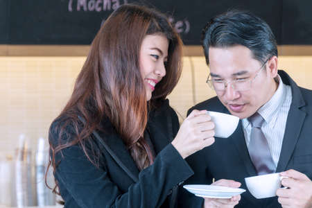 Couple business sitting in coffee shop. Cheerful young woman holding cup of coffee in her hand while...