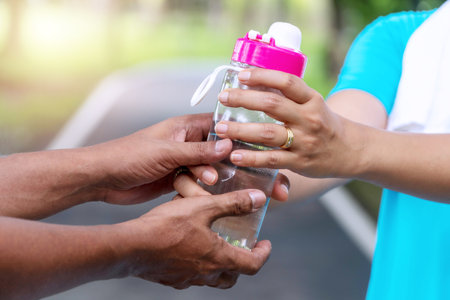 Hands of senior man holding bottle of fresh water for his wife while workout in the park. Healthy lifestyle concept.の写真素材