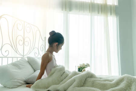Sweet little girl wake up in the morning at home. Cheerful kid girl with flower sitting on white bed. Lifestyle concept.の写真素材