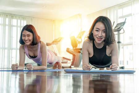 Attractive young cheerful asian woman wearing sportswear with push up arm together in fitness center. Two fitness slim female friend workout bodybuilding in gym. concept of exercise.の写真素材