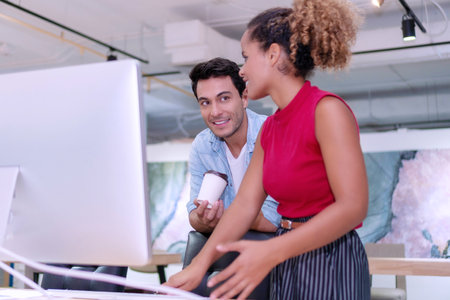 Two businesspeople colleagues talking about planning project in the workplace. Woman and man standing with computer talking work together in office.の写真素材