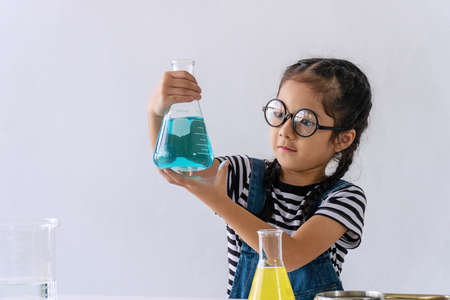 Little 6s cute girl with microscope holding laboratory bottle with water experiment study scientists at school. Education science concept.の写真素材
