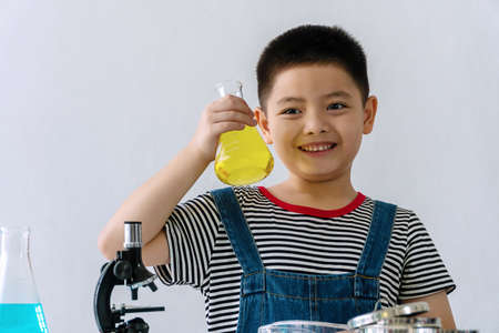 Little cute boy with microscope holding laboratory bottle with water experiment study scientists at school. Education science concept.の写真素材