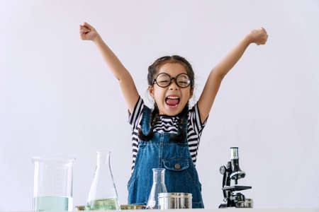 Little 6s cute girl wear glasses happy raise arms with microscope, laboratory bottle and water experiment study scientists while learning success at school. Education science concept.の写真素材