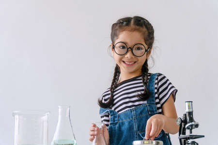 Little 6s cute girl smiling with microscope, laboratory bottle and water experiment study scientists while looking camera at school. Education science concept.の写真素材