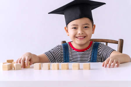 Little cute boy concentrate wooden block on table while sitting in the white room. Adorable pigtails...