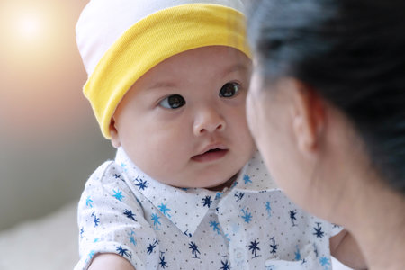 Innocent little cute boy looking at his mother while mom embrace his in arms at home. Eye of cute childhood looking at his parent with love. Mothers day concept.の写真素材