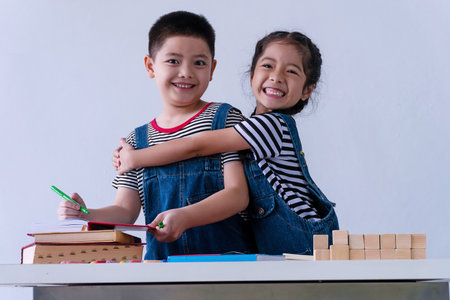 Innocence little cute girl smiling with wooden block and book on table while embracing her brother on white background. Brotherhood hugging together feeling happiness. Relationship sibling concept.の写真素材
